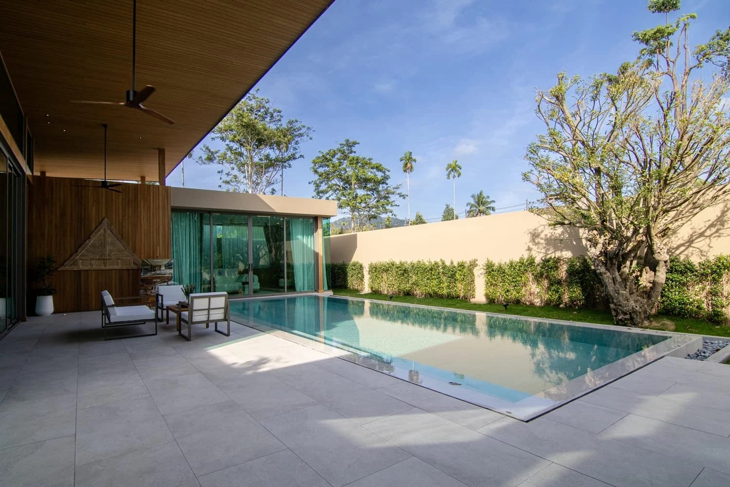Mustervilla A1: der 12 m lange Pool, die holzverkleidete Terrasse und der alte Baum unter klarem Himmel