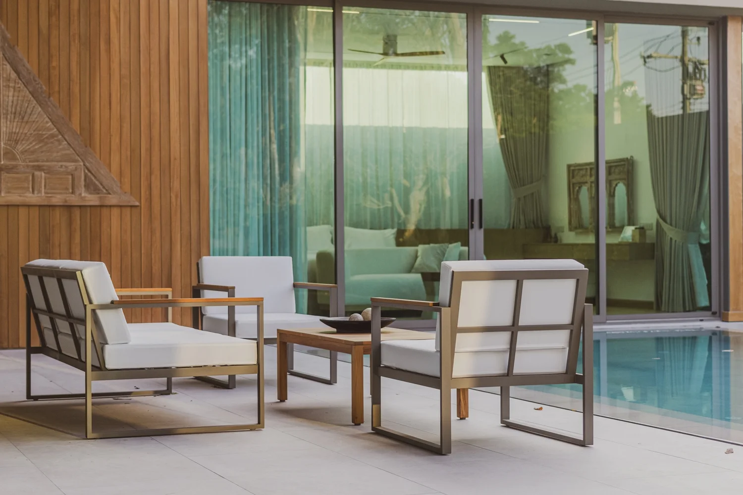 Teak-Loungesessel vor der Wand aus senkrechtem Holz mit geschnitztem Thai-Giebel